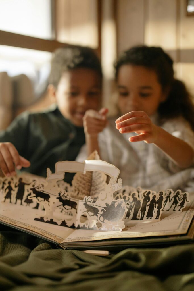 Two children enjoying a Christmas pop-up book indoors, sharing joyful moments.